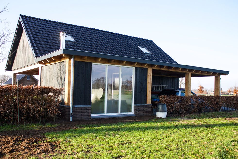 Bijgebouw in zwart hout met douglas overkapping en schuifpui, gezien vanuit de tuin